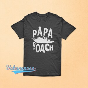 Puede incluir: Una camiseta gris oscuro con un estampado gráfico blanco de un barco y el texto "Papa Roach".
