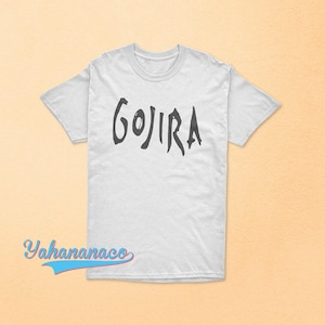 Op de afbeelding: Een wit T-shirt met korte mouwen en het woord GOJIRA in een donker, gestileerd, handgetekend lettertype op de borst gedrukt. Het T-shirt heeft een ronde hals en een standaard pasvorm. De tekst Yahanaco is zichtbaar in de linkerbenedenhoek.