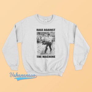 May include: A white sweatshirt with a black and white photo of a man being arrested by a police officer. The text "Rage Against The Machine" is printed on the sweatshirt.
