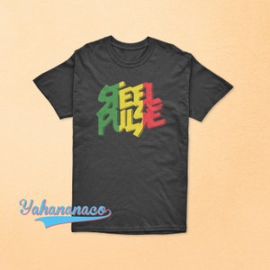 以下が含まれることがあります： 緑、黄色、赤で「Steel Pulse」と書かれたダークグレーのTシャツ
