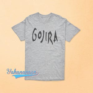 Op de afbeelding: Een grijs gem&ecirc;leerd T-shirt met korte mouwen en het woord GOJIRA in een donker, gestileerd en grillig zwart lettertype op de borst gedrukt. Het kledingstuk heeft een standaard ronde hals en een rechte zoom voor een eenvoudig ontwerp.