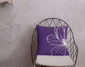 May include: Purple throw pillow with a white floral design. The pillow is sitting on a black metal chair.