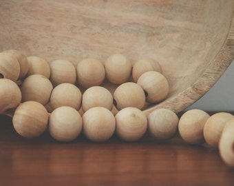 May include: A wooden bowl filled with a string of natural wood beads. The beads are light brown and have a smooth, polished finish.