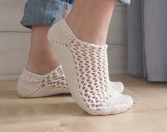 May include: A pair of off-white, low-cut ankle socks featuring a delicate, open-work knit pattern across the top of the foot and a solid knit heel and toe section. The socks are crafted from a light-colored yarn and sit just below the ankle bone.