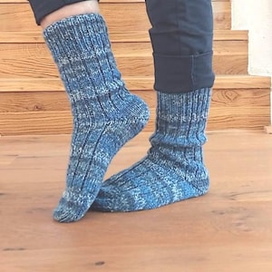 May include: A pair of blue and white knit socks with a ribbed cuff. The socks are worn with black pants. The socks are made of a soft, textured yarn and appear to be hand-knitted. The socks are a medium length and cover the ankles.
