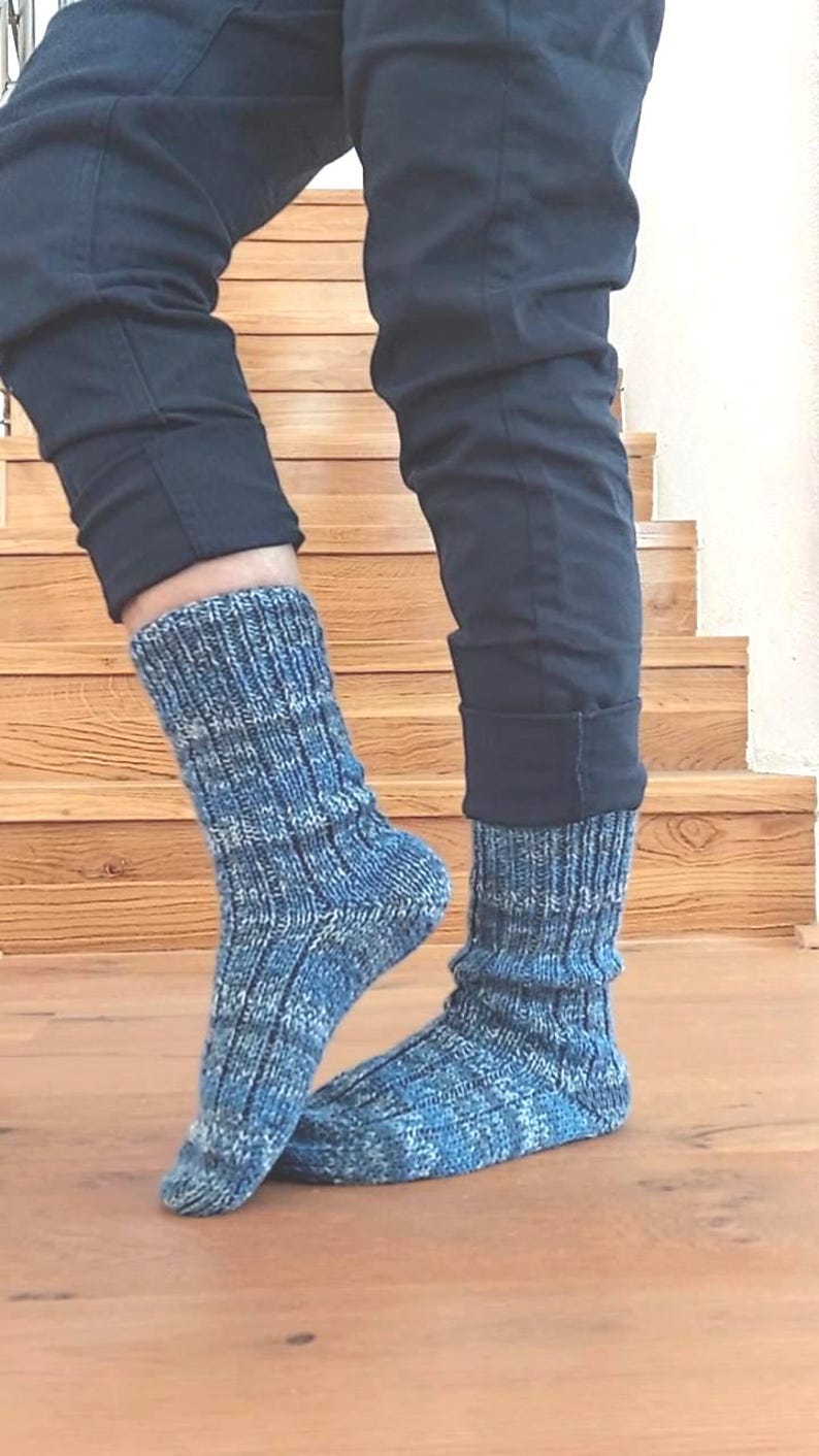 Puede incluir: Un par de calcetines de punto azul y blanco con un pu&ntilde;o acanalado. Los calcetines se llevan con pantalones negros. Los calcetines est&aacute;n hechos de un hilo suave y texturizado y parecen estar tejidos a mano. Los calcetines son de longitud media y cubren los tobillos.