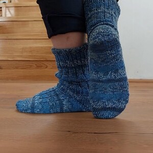 Puede incluir: Un par de calcetines azules de punto con un patr&oacute;n texturizado. Los calcetines presentan una mezcla de tonos azules claros y oscuros, con un pu&ntilde;o acanalado. Los calcetines est&aacute;n sobre un suelo de madera.