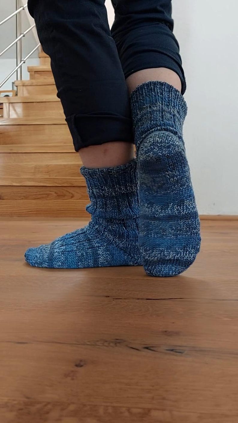 Puede incluir: Un par de calcetines azules de punto con un patr&oacute;n texturizado. Los calcetines presentan una mezcla de tonos azules claros y oscuros, con un pu&ntilde;o acanalado. Los calcetines est&aacute;n sobre un suelo de madera.