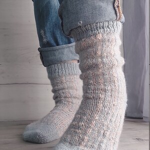 May include: A pair of light blue and peach knitted socks. The socks are worn with blue denim jeans with rolled-up cuffs. The socks have a textured pattern and are made of soft yarn.