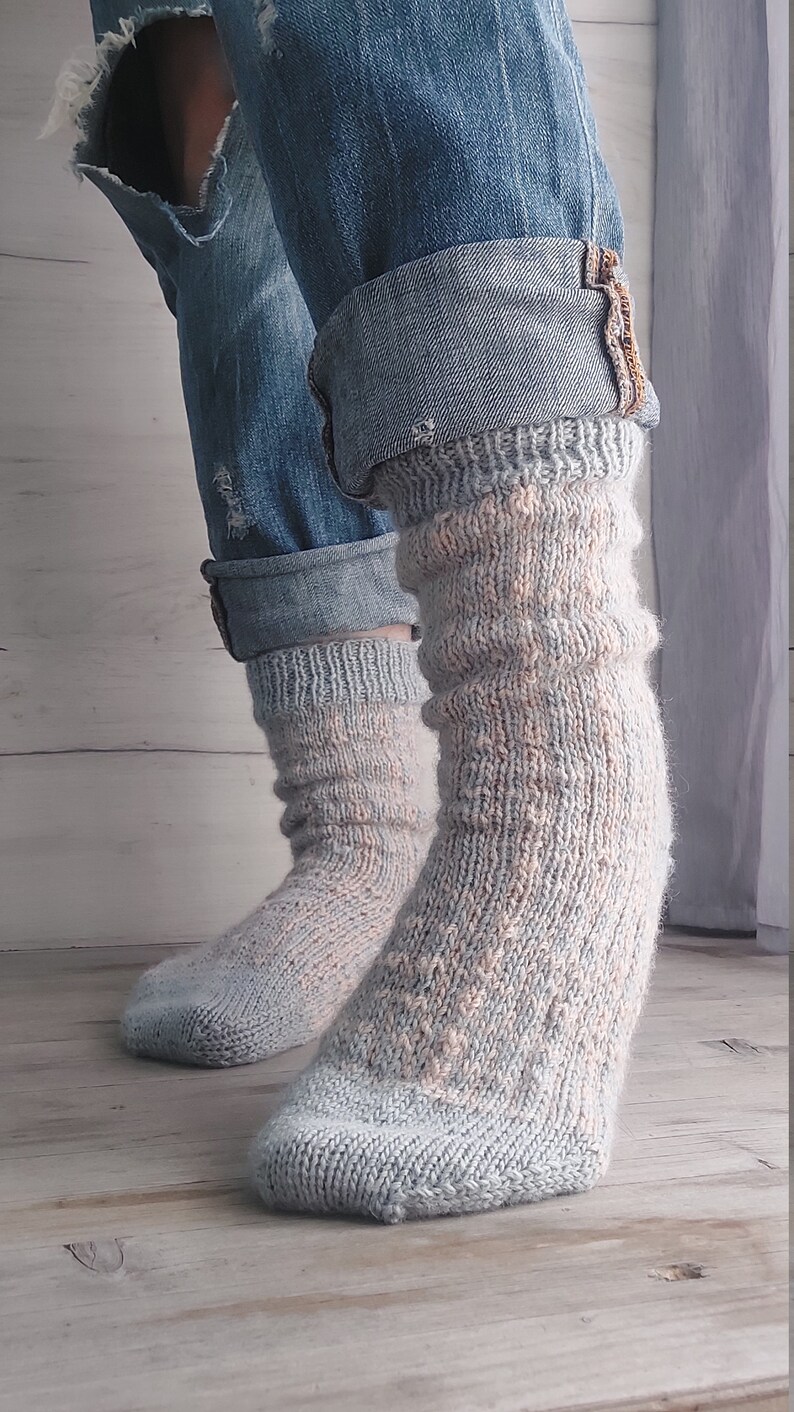 May include: A pair of light blue and peach knitted socks. The socks are worn with blue denim jeans with rolled-up cuffs. The socks have a textured pattern and are made of soft yarn.