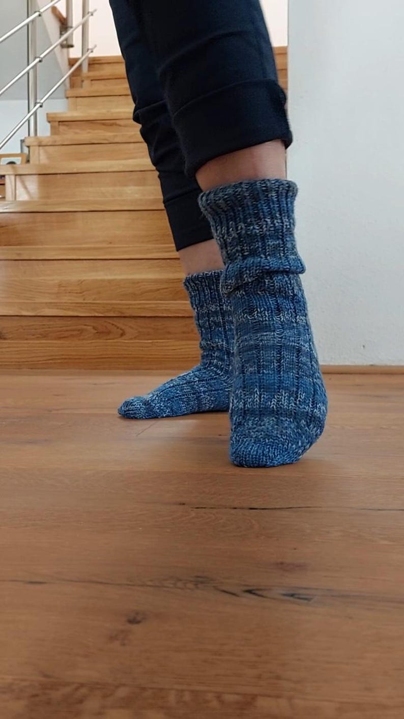 Puede incluir: Un par de calcetines azules de punto con un patr&oacute;n texturizado. Los calcetines se llevan con pantalones oscuros y est&aacute;n sobre un suelo de madera. Los calcetines son una mezcla de hilos azules y blancos.