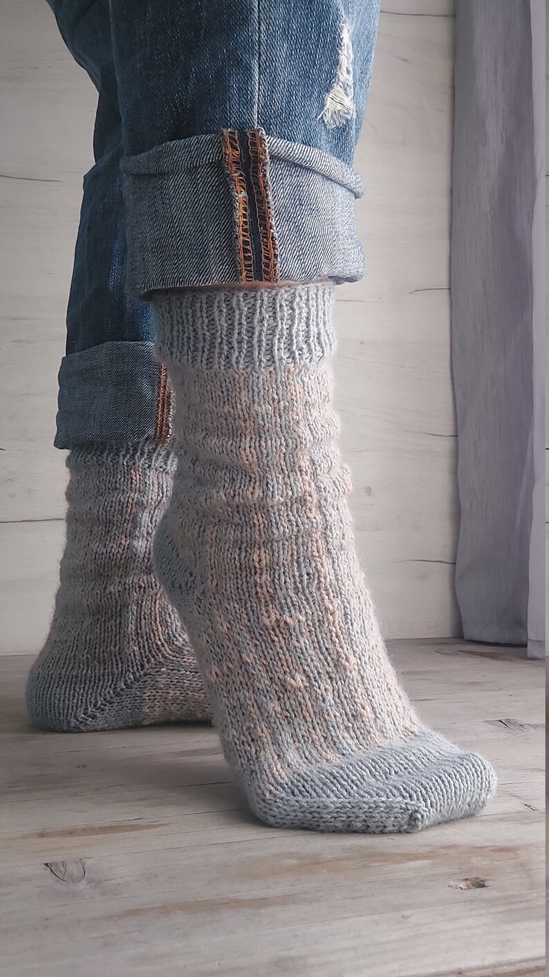 May include: A pair of light blue and peach-coloured knitted socks. The socks are worn with rolled-up denim jeans. The socks have a textured pattern and are made of a soft, warm material. The jeans have a distressed look.