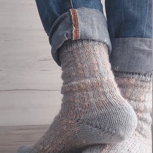 May include: A pair of light blue and peach-coloured knitted socks. The socks are worn with blue denim jeans, cuffed at the ankles. The socks have a textured pattern and are made of a soft, warm material.