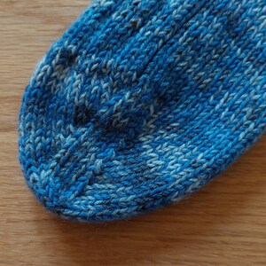 Puede incluir: Primer plano de un calcet&iacute;n tejido azul y blanco. El calcet&iacute;n est&aacute; hecho de un hilo texturizado con un patr&oacute;n de costillas. Los colores son tonos de azul y blanco, creando una apariencia texturizada. El calcet&iacute;n est&aacute; sobre una superficie de madera.