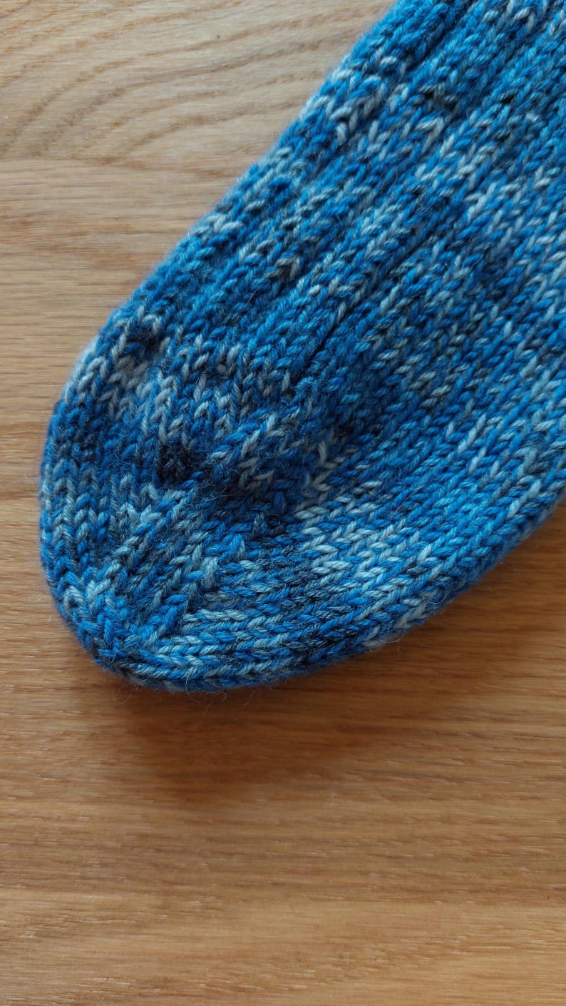 Puede incluir: Primer plano de un calcet&iacute;n tejido azul y blanco. El calcet&iacute;n est&aacute; hecho de un hilo texturizado con un patr&oacute;n de costillas. Los colores son tonos de azul y blanco, creando una apariencia texturizada. El calcet&iacute;n est&aacute; sobre una superficie de madera.