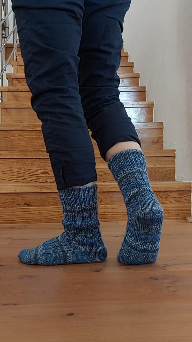 Puede incluir: Un par de calcetines de punto azules con un patr&oacute;n texturizado. Los calcetines se usan con pantalones azul oscuro, y el fondo presenta escaleras y pisos de madera.