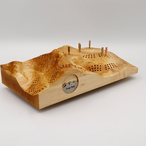 May include: A wooden game board shaped like a mountain range with holes and pegs. The board is made of light wood and has a metal plaque that says "Lange Peak".