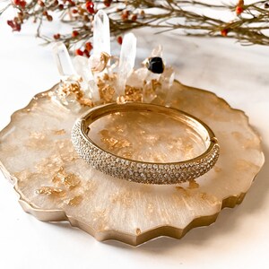 May include: A gold ring holder with a white agate base and gold leaf accents. The holder features a crystal ring stand and a gold bangle with clear rhinestones.