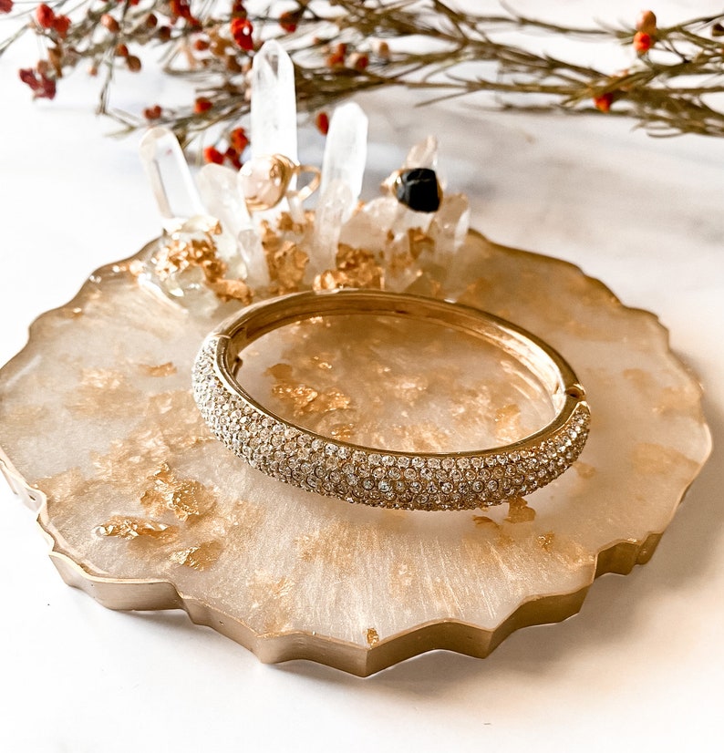 May include: A gold ring holder with a white agate base and gold leaf accents. The holder features a crystal ring stand and a gold bangle with clear rhinestones.