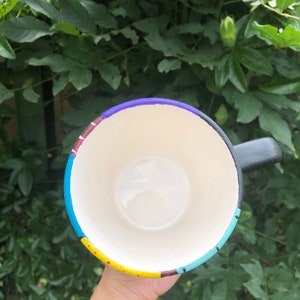 Peut inclure: Une tasse &agrave; caf&eacute; noire avec un motif peint color&eacute;. Le motif pr&eacute;sente des rayures et des points jaunes, bleus, rouges, violets et blancs.