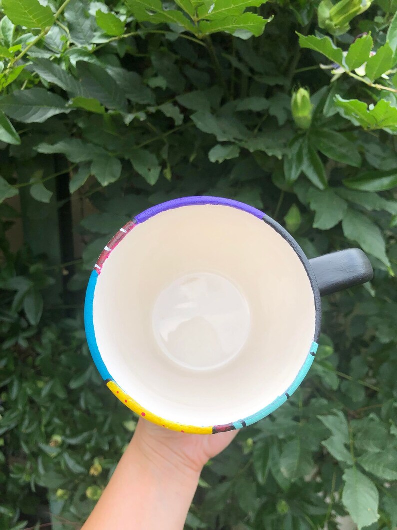Peut inclure: Une tasse &agrave; caf&eacute; noire avec un motif peint color&eacute;. Le motif pr&eacute;sente des rayures et des points jaunes, bleus, rouges, violets et blancs.