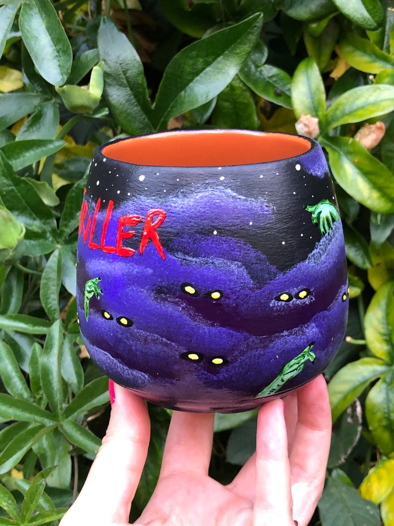 K&ouml;nnte beinhalten: Handbemalte Keramiktasse mit einem dunkelvioletten und schwarzen Nachthimmel-Design. Das Wort "KILLER" ist rot geschrieben. Die Tasse hat gelbe Augen und gr&uuml;ne, au&szlig;erirdische Figuren. Der Innenraum ist orange.