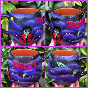 K&ouml;nnte beinhalten: Handbemalte Keramik-Tasse mit lila Griff und Innenraum. Die Tasse zeigt ein Nachthimmel-Design mit dem Wort "Thriller" in Rot, einer Zombie-Figur und gr&uuml;nen Zombie-H&auml;nden. Die Tasse ist ein einzigartiges Kunstwerk.
