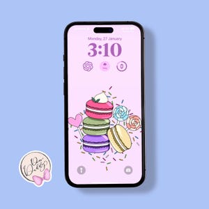 Puede incluir: Una pantalla de teléfono rosa y blanca con un reloj digital que muestra las 3:10, la fecha del lunes 27 de enero y una pila de macarons coloridos con chispas y piruletas.