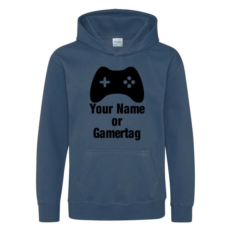 以下が含まれることがあります： 黒いビデオゲームコントローラーのグラフィックと「Your Name or Gamertag」というテキストが書かれた濃い青色のフード付きスウェットシャツです。