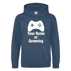 以下が含まれることがあります： 白いビデオゲームコントローラーのグラフィックと「Your Name or Gamertag」というテキストが書かれたネイビーブルーのフード付きスウェットシャツです。