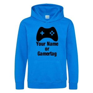 以下が含まれることがあります： 黒いビデオゲームコントローラーのグラフィックと「Your Name or Gamertag」というテキストが書かれた明るい青色のフード付きスウェットシャツです。