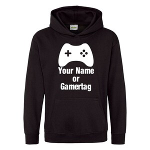 以下が含まれることがあります： 白いビデオゲームコントローラーのグラフィックと「Your Name or Gamertag」というテキストが書かれた黒いフード付きスウェットシャツ。