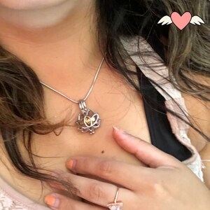May include: A silver-colored necklace with a lotus flower pendant. The pendant has a cage-like design with a yellow center. The necklace is worn on a person's neck.