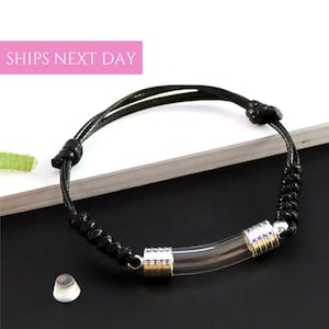 May include: A black cord bracelet with a clear glass tube charm. The tube is capped with silver metal on both ends.