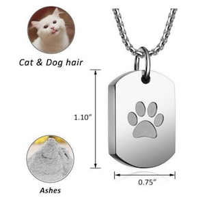 May include: Silver paw print cremation pendant necklace with a chain. The pendant is 1.10 inches tall and 0.75 inches wide. It can hold ashes, cat or dog hair.