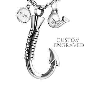 May include: Silver fishing hook necklace with a small round charm that says "Customize it" and a fish charm. The necklace is on a silver chain. The hook is detailed with a spiral design. The text "CUSTOM ENGRAVED" is displayed below the necklace.