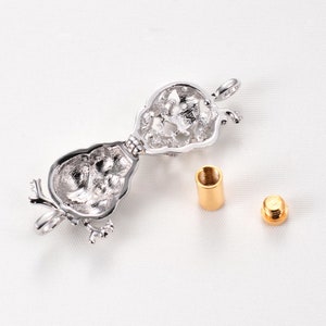 May include: Silver tone openable locket pendant with a detailed design. The locket is open and shows the inside. Two gold tone metal pieces are also shown.
