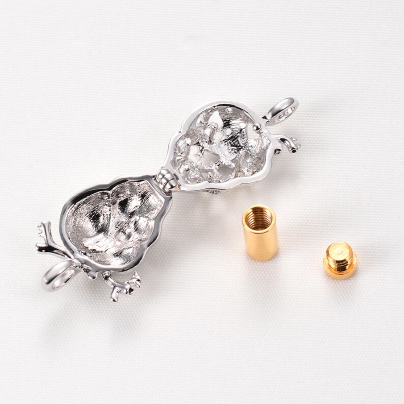 May include: Silver tone openable locket pendant with a detailed design. The locket is open and shows the inside. Two gold tone metal pieces are also shown.