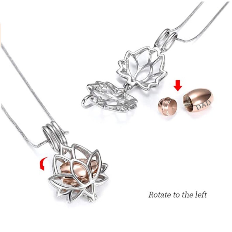 May include: A silver-colored lotus flower pendant necklace with a rose gold urn inside. The pendant opens to reveal the urn, which is engraved with the word "DAD". The necklace is displayed on a white background.