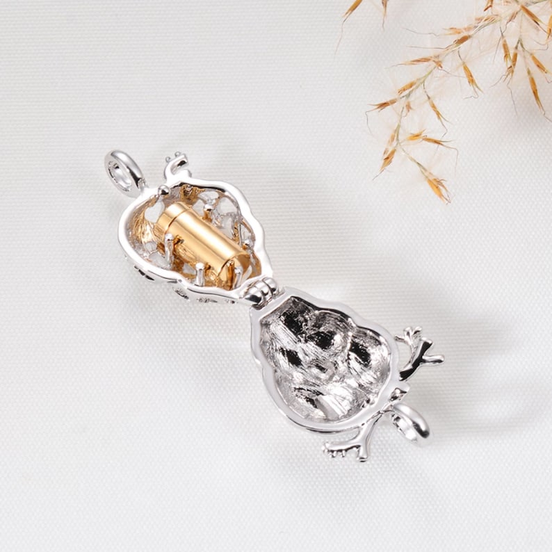 May include: Silver tone pendant necklace with a small, open, heart-shaped locket. The locket is open and a small, gold-tone cylinder is inside. The pendant is attached to a silver tone chain.