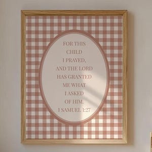 May include: A framed print with the text "FOR THIS CHILD I PRAYED, AND THE LORD HAS GRANTED ME WHAT I ASKED OF HIM 1 SAMUEL 1:27" in an oval shape, set against a pink and white gingham pattern. A wicker chair with a teddy bear and a crib are also visible.
