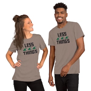 Puede incluir: Dos personas vistiendo camisetas color taupe. Cada camiseta presenta el texto "LESS THINGS" en letras negras, con tres gráficos de cocodrilos verdes encima de "THINGS". Las camisetas son de manga corta.