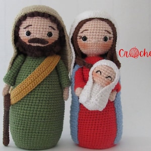 May include: Crocheted figures of the Holy Family: Joseph, Mary, and baby Jesus. Joseph is wearing a green robe with a brown staff and a yellow sash. Mary is wearing a red robe with a blue outer garment and holding baby Jesus wrapped in white. The figures are handmade and have a sweet, whimsical style.