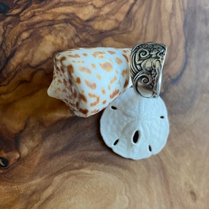 May include: A silver ring with an intricate design featuring a woman's face and floral motifs. The ring is displayed on a seashell and a sand dollar.