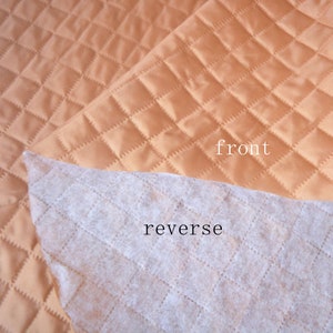 May include: A close-up of a quilted fabric with a diamond pattern. The fabric is a light brown color. The front side of the fabric is smooth and shiny, while the reverse side is a soft, white, non-woven fabric. The text "front" and "reverse" is visible on the image.