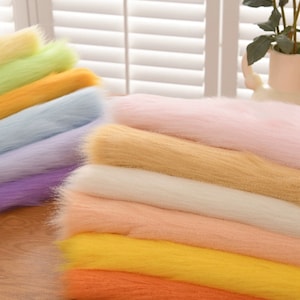May include: A stack of colourful wool roving in shades of light green, yellow, blue, purple, pink, white, peach, yellow, and orange. The wool is arranged in a rainbow pattern.