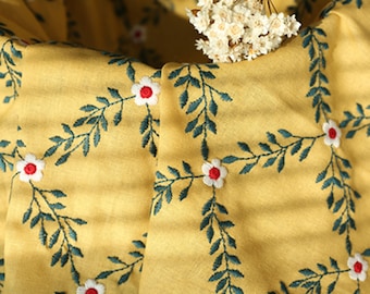 May include: Yellow fabric with an embroidered pattern of white flowers with red centers and green leaves.