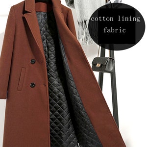 May include: A brown double-breasted wool coat with a black quilted cotton lining. The coat is open and the lining is visible. The coat is hanging on a black coat rack.