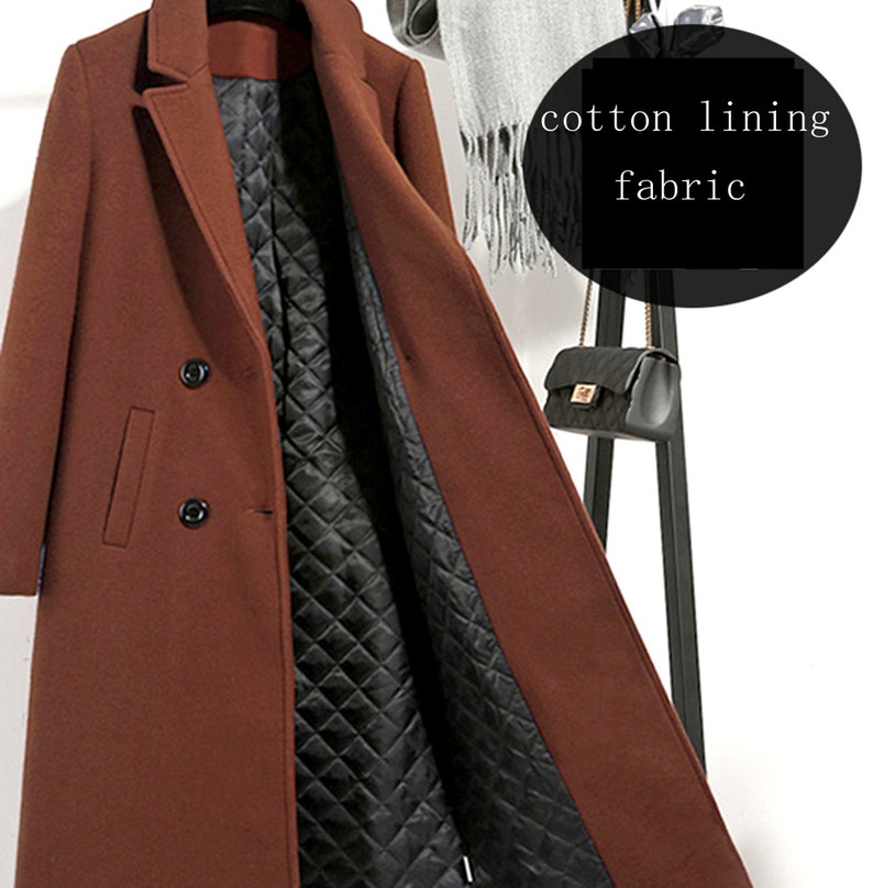 May include: A brown double-breasted wool coat with a black quilted cotton lining. The coat is open and the lining is visible. The coat is hanging on a black coat rack.