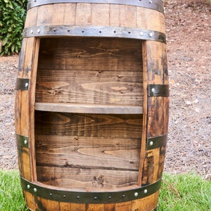 May include: A wooden barrel shelf with two shelves. The barrel is brown with black metal bands and rivets. The shelves are made of wood and are empty.